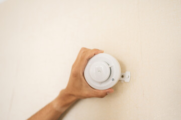 Close-up hands of unrecognizable electrician mounting smoke detector on wall, ensuring safety and...