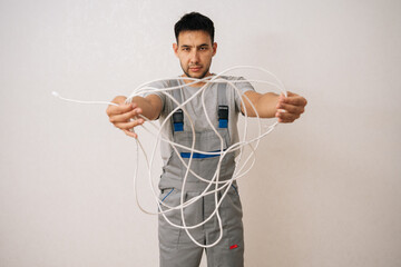 Front view of skilled electrician male wearing grey uniform holding bunch of tangled white...