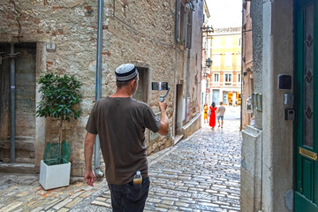 Man filming cobblestone street in old European town. A tourist with smartphone gimbals records...