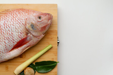 Red Tilapia fish head and Galangal, lemongrass, kaffir lime leaves on a wooden board on a white background. with copy space