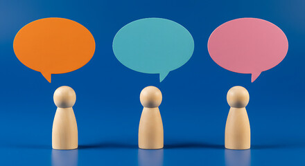 Obraz premium Three wooden figures stand beneath vibrant speech bubbles against a blue backdrop, symbolizing collaborative discussions and communication, ideas