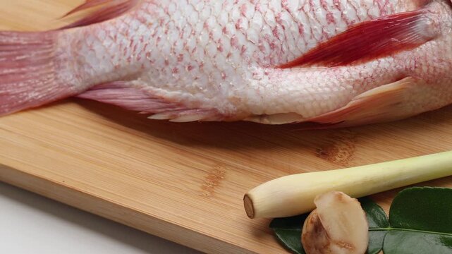 Side view One fresh Red Tilapia fish and Galangal, lemongrass, kaffir lime leaves on a wooden board