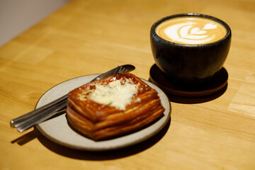 Cup of hot milk latte coffee and Mushroom danish pastry on table.