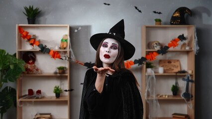 Vampire witch blows a kiss in a room decorated for Halloween