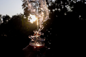 Sparkling Water Poured Over Stacked Glass Bottles, Sunlight Backlighting Splashes and Bubbles in Natural Setting