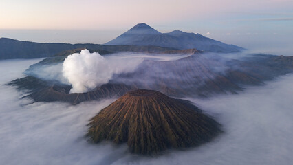 Aerial view of Mount Bromo volcano at sunrise surrounded by clouds and mist in East Java, Indonesia. Scenic volcanic landscape with smoke, mountains, and dramatic sky.