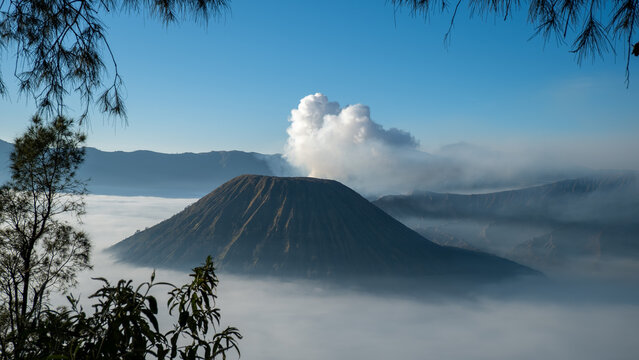 Aerial view of Mount Bromo volcano at sunrise surrounded by clouds and mist in East Java, Indonesia. Scenic volcanic landscape with smoke, mountains, and dramatic sky. - Powered by Adobe