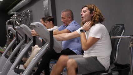 Men and woman taking indoor cycling class at fitness center, doing cardio riding bike - Powered by Adobe
