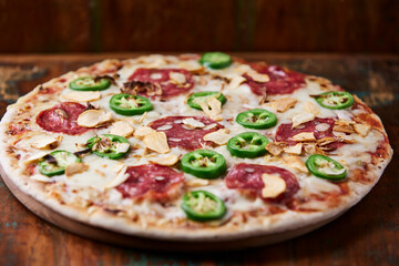 Pizza with salami, mozzarella cheese and jalapeno pepper. Wooden background. Soft focus.	
