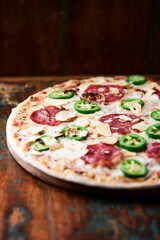 Pizza with salami, mozzarella cheese and jalapeno pepper. Wooden background. Soft focus.	