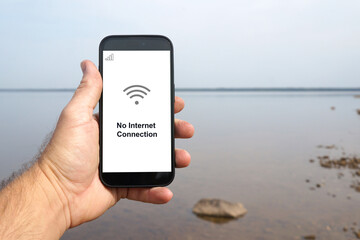 Hand holding smartphone displaying no internet connection by the lake