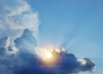 The sun and sun rays appearing from behind a great fluffy cloud.