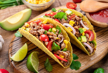 Mexican meat tacos or beef stuffed tortillas and lime slices near them on wooden serving board.