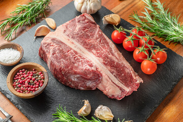 Raw T-bone steak with seasonings on slate serving plate. Flat lay.