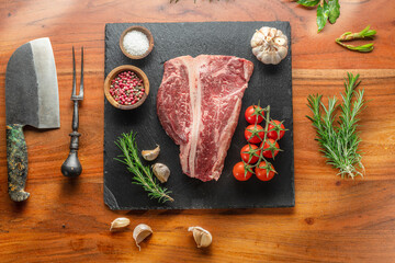 Raw T-bone steak with seasonings on slate serving plate. Flat lay.