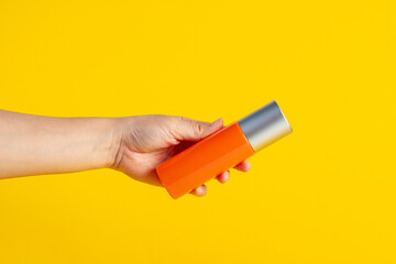 Skin care or sunscreen cosmetic with hand on yellow background.