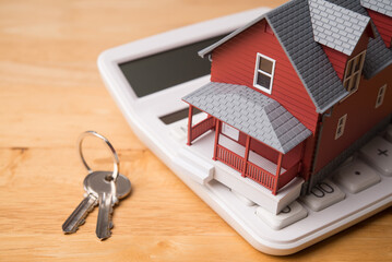 Red house model on white calculator and house key on wooden table background. Homebuyers, mortgage...