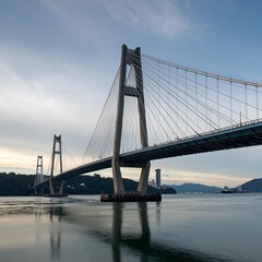 Obraz premium A substantial cable-stayed bridge spans a calm waterway, reflecting the structure's imposing form on the glassy surface.