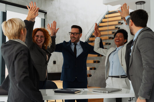 Group of business people in office raising hands and celebrating success. Happy colleagues cheering together, teamwork, achievement, and corporate victory concept.
