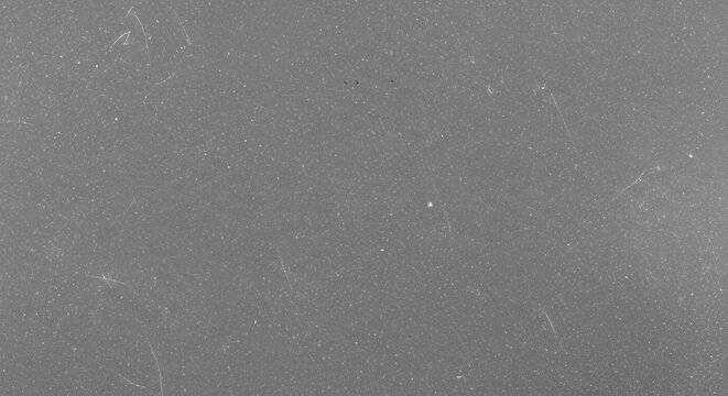 A macro photograph of a flat, solid gray surface showing subtle texture, faint scratches, and dust particles.