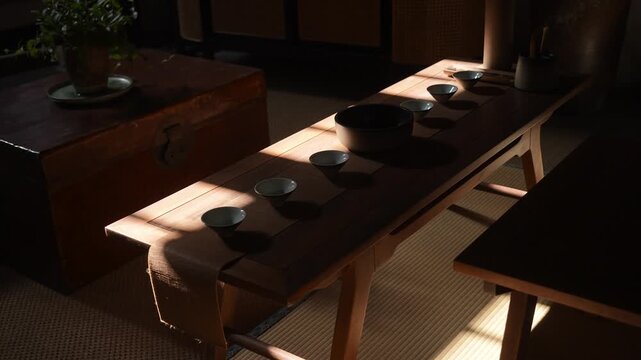 Wooden tea table with traditional tea utensils arranged in a serene indoor setting with natural light and shadow play