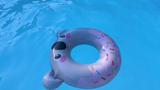 Cute inflatable sloth pool float with colorful sprinkles pattern floating on crystal clear blue swimming pool water - summer vacation and relaxation concept
