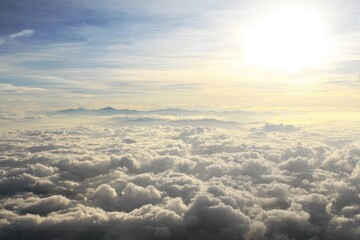 Expansive view of a sunlit sky above a vast sea of fluffy clouds with distant mountains