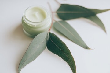 Pale green cream jar with eucalyptus leaves on white background