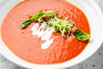 Gourmet tomato soup served in a bowl, garnished with fresh basil, shredded zucchini, and cream...