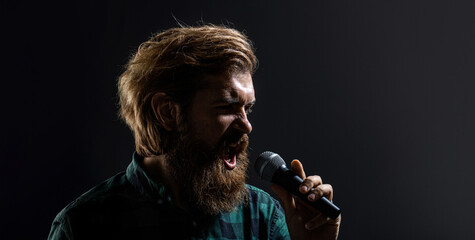 Man with a beard holding a microphone and singing. Bearded man in karaoke sings a song into a microphone. Male singing with a microphones. Male attends karaoke. Bearded man singing with microphone
