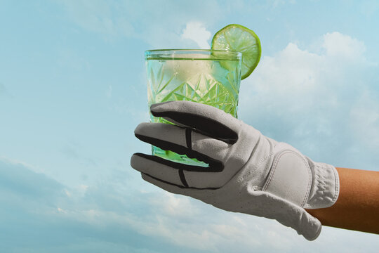 Hand in golf glove holding green cocktail glass with lime against blue sky vibrant mood. Concept of summer refreshment, lifestyle branding, leisure culture and beverage promotion.