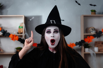 Vampire witch in a black cloak and hat pointing upwards