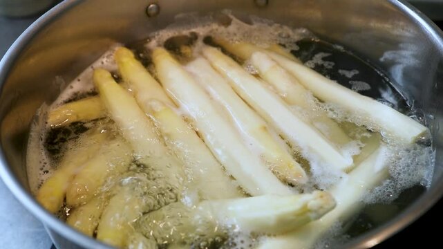 Botte d'asperges blanches fraichement &eacute;pluch&eacute;es en train de cuire dans une casserole d'eau en &eacute;bullition. Sc&egrave;ne culinaire - France.