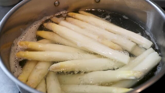 Botte d'asperges blanches fraichement &eacute;pluch&eacute;es en train de cuire dans une casserole d'eau en &eacute;bullition. Sc&egrave;ne culinaire - France.