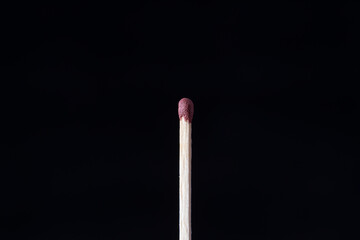 a single matchstick standing upright against a completely dark, black background