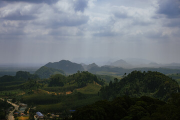A misty landscape with layers of green hills and mountains under dramatic clouds, wide panoramic...