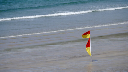 Red and yellow flag on a sandy beach signals safe swimming area under