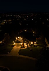Night view of a brightly lit house in a suburban neighborhood.