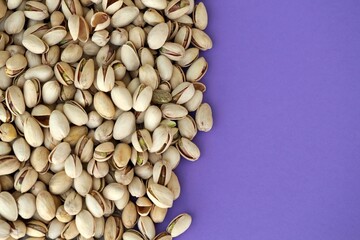 Tasty unpeeled pistachios on bright purple background, top view flat lay background pattern