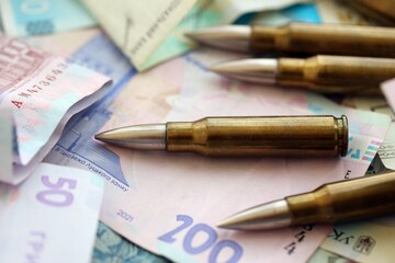 Many rifle bullets lies on lots of ukrainian money bills close up