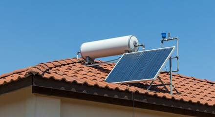 Solar water heater system installed on a tiled roof with a clear blue sky as the background scenery