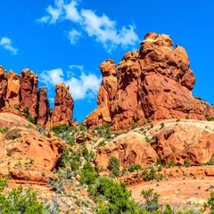 Fototapeta premium A vibrant landscape showcasing dramatic red rock formations against a cerulean sky dotted with fluffy white clouds.