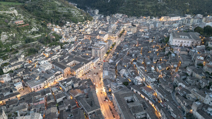 Modica by night – winding streets glowing with golden lights, baroque houses climbing the...