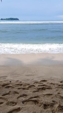 Footprints on a sandy beach with gentle waves at Angso Duo Island, Pariaman, Indonesia, showing traces of visitors enjoying the coastline