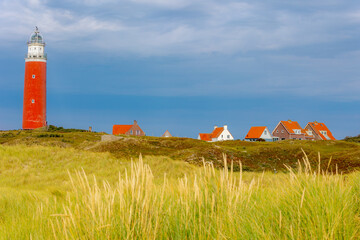 The Eierland Lighthouse on the northernmost top of the Dutch island of Texel, Red lighthouse tower on the sand dunes with european marram grass under blue sky, De Cocksdorp, North Holland, Netherlands