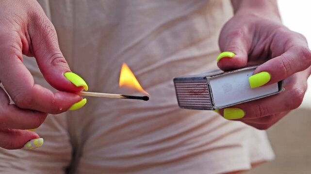 Slow motion shot of woman holding burning matchstick with glowing orange flame
