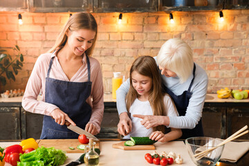 Young beautiful woman with her daughter and mother cooking salad in kitchen. The family spends time...