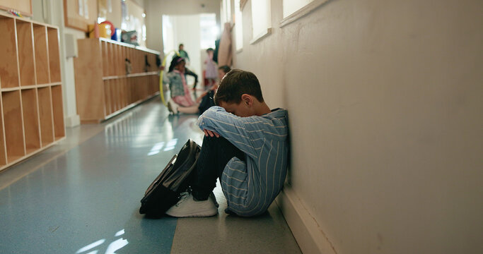 Boy, sad and depressed in corridor at school, alone and social isolation with mental health on floor. Child, anxiety and bullying in hallway with profile, frustrated or crying with stress at academy