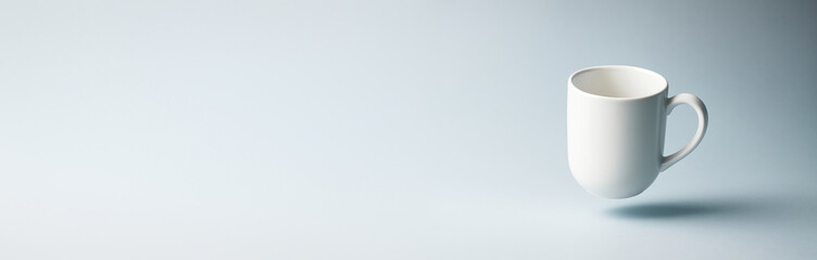 Fototapeta premium Minimalistic white coffee mug floating on light gradient background with empty copyspace for clean design, banner, poster or product mockup. Ai generative