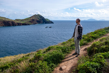 Young man stands on volcanic cliff edge Madeira island, hiking adventure, cliffside trail, gazing...